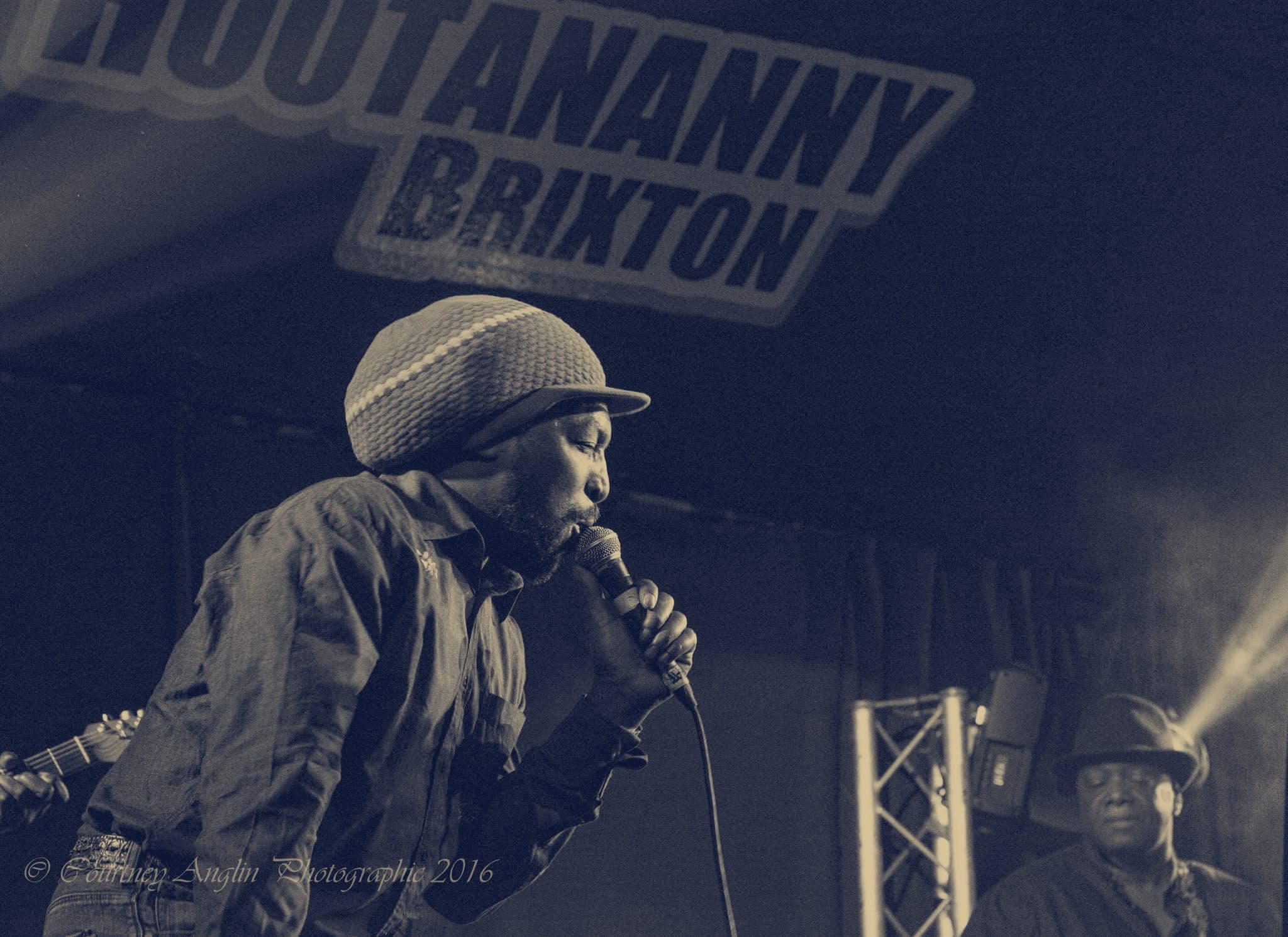 Kareem Shabazz singing in a knitted cap under the Hootananny Brixton sign, in black and white